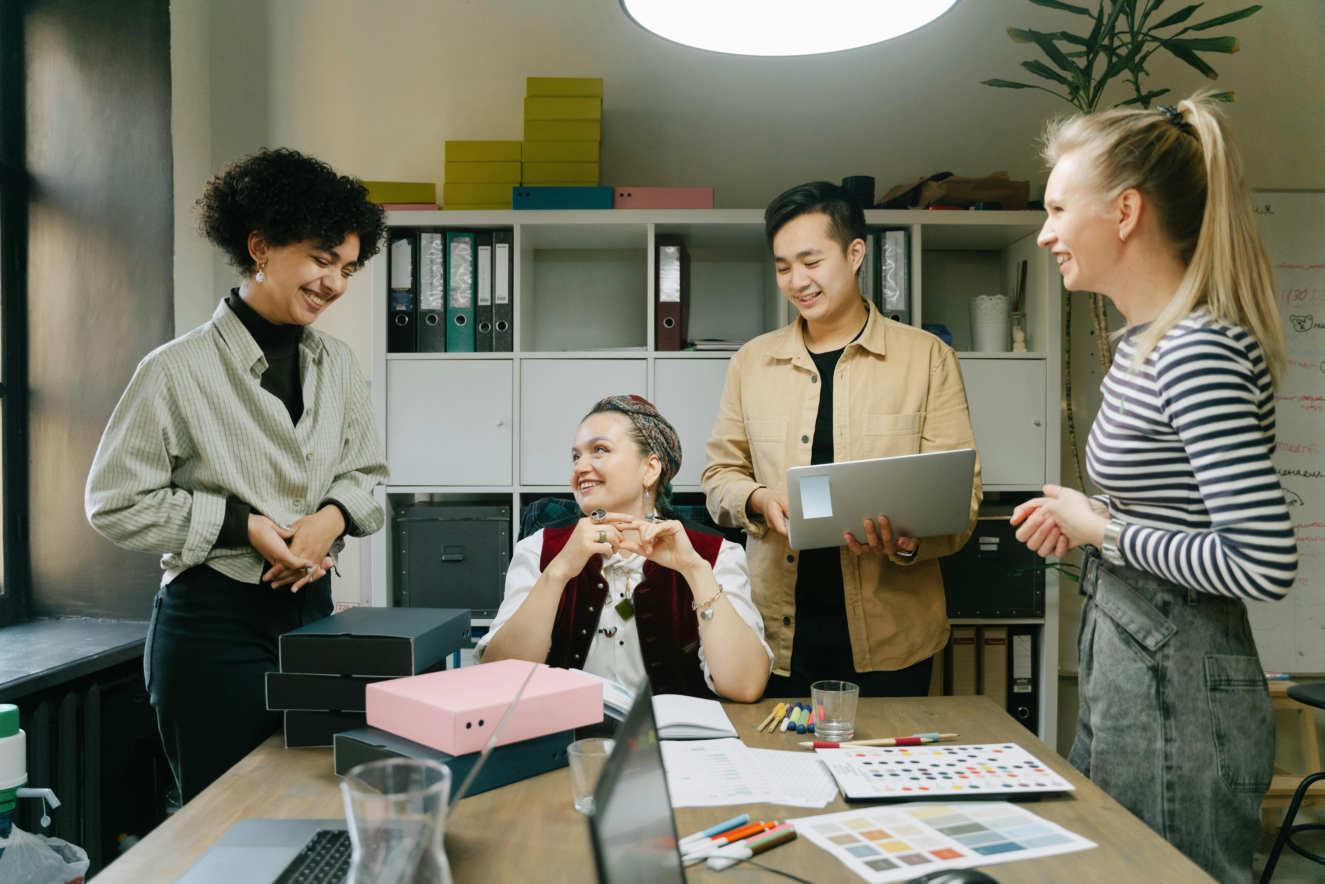 Four employees sitting around a desk smiling and working on lab tops looking very engaged 